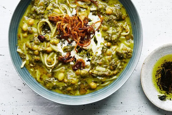 A bowl of Aash Reshteh — a thick green noodle and bean soup topped with a swirl of whey, fried onions and mint