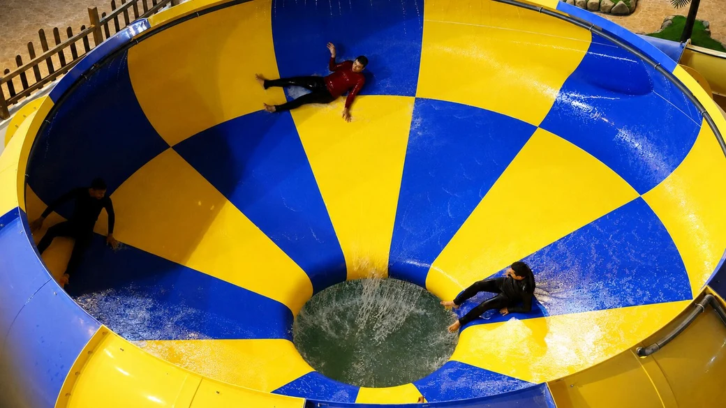 Riders sliding around the giant blue-and-yellow tornado bowl at the Abotab water park, seen from above