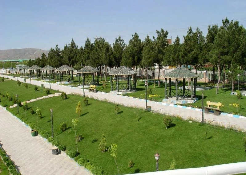 Neat green lawns and rows of shaded gazebos among tall pines at Alavi Park, with hills in the distance