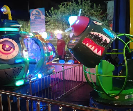 Monster-faced children's rides lit in green and purple at an indoor amusement park at night