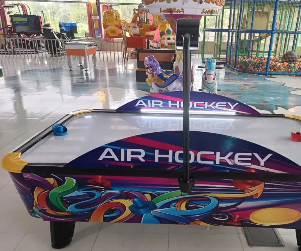 An air-hockey table in an indoor amusement park, with a carousel and a ball pit behind it