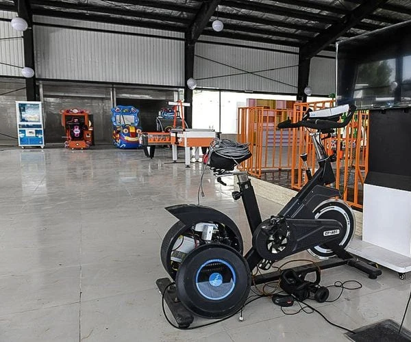 A virtual-reality exercise bike wired to a screen in an open steel-framed indoor play hall