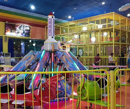 A rocket-themed children's ride in front of a multi-storey soft-play climbing cage