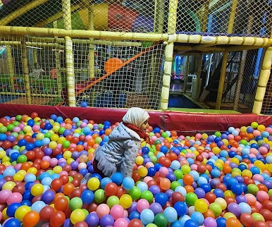 A child in a headscarf wading through a large pit of multicoloured plastic balls in the soft-play area