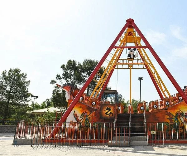 A dragon-painted pirate-ship swing on its red A-frame at an outdoor amusement park in Qum