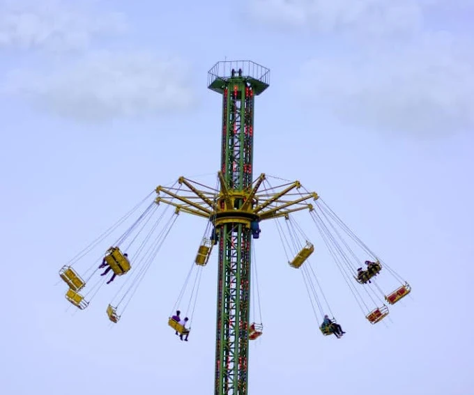 A green star-flyer swing tower carrying seated riders high above the park at dusk