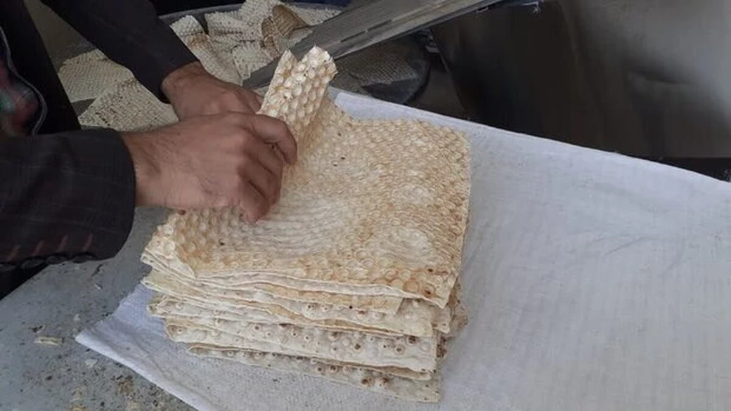 A tall stack of thin, soft Lavash flatbread, with a baker lifting a sheet from the top