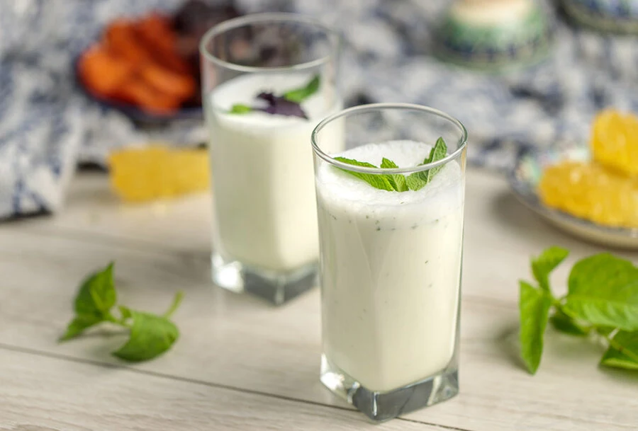 Two tall glasses of Doogh — a frothy white yoghurt drink — each topped with a sprig of fresh mint