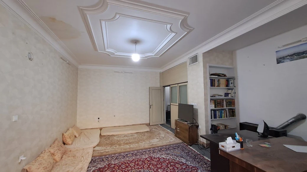 A furnished common room in the SIOS dormitory, with floor cushions, a Persian carpet, a television, a bookshelf and a study desk
