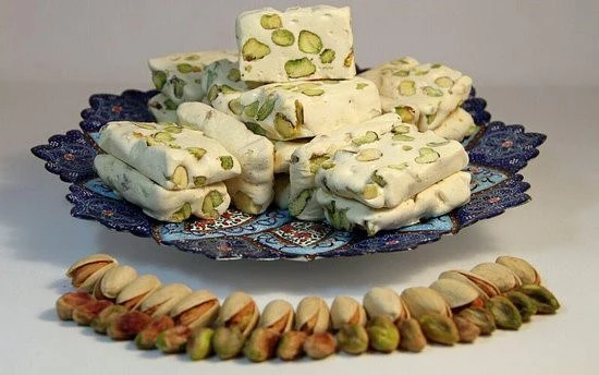 A plate of Gaz — Iranian nougat studded with whole pistachios — beside a row of pistachios
