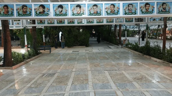 The tree-lined walkway through Gulzar Shuhada in Qum, its marble paving inscribed with the names of the martyrs buried beneath, with portrait boards of the fallen hung overhead