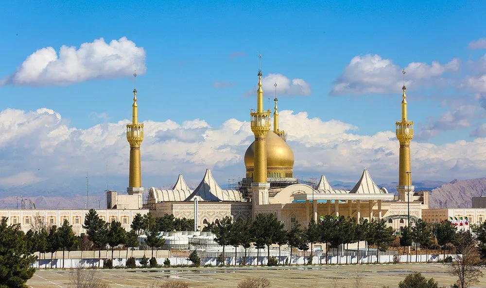 The Mausoleum of Imam Khumayni on the outskirts of Tehran, a vast complex with a large golden dome flanked by four tall golden minarets under a blue sky