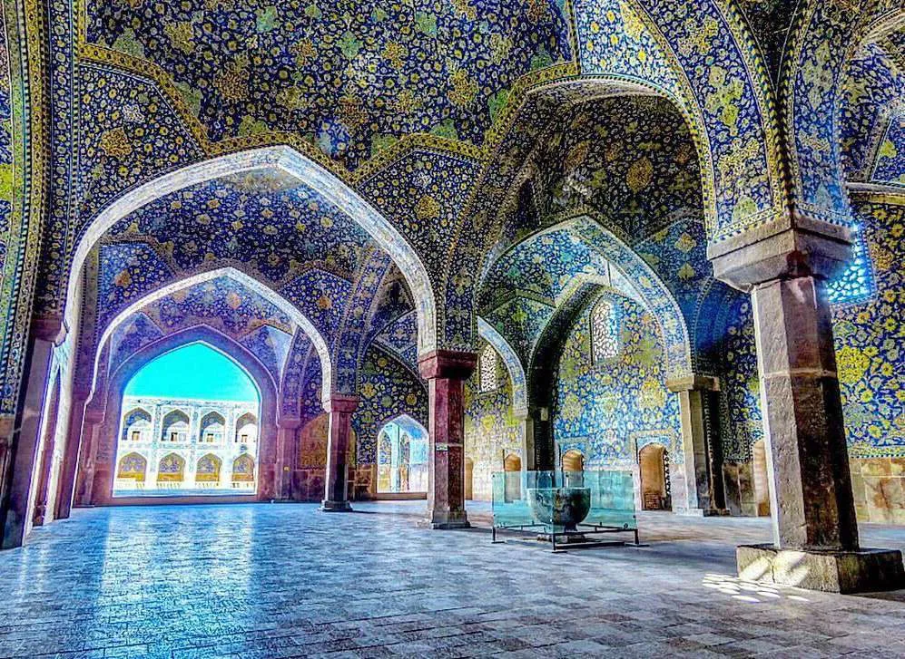 The interior of the Abbasi Jami (Imam) Mosque in Isfahan, with soaring arches and columns entirely covered in intricate blue, turquoise and gold floral tile mosaics