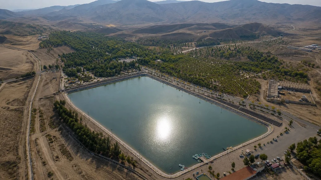 An aerial view of the large rectangular man-made lake at Javan Park, ringed by young planting with the arid hills of Qum behind