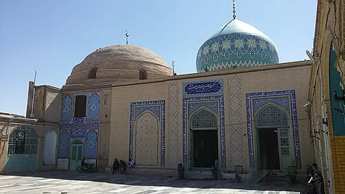 The exterior of the shrine of Musa al-Mubarqa' in Qum, its turquoise tiled dome rising beside a plain brick dome above a tiled portal