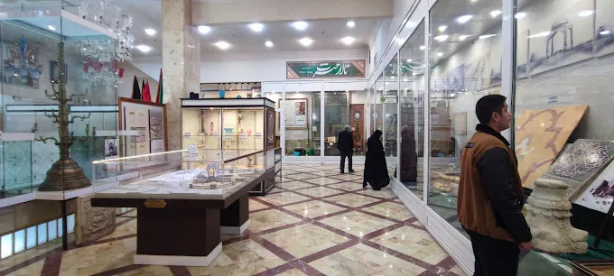 An interior hall of the Lady Masumah (a) Museum, lined with glass display cases of historical artefacts under a marble-floored gallery as visitors browse