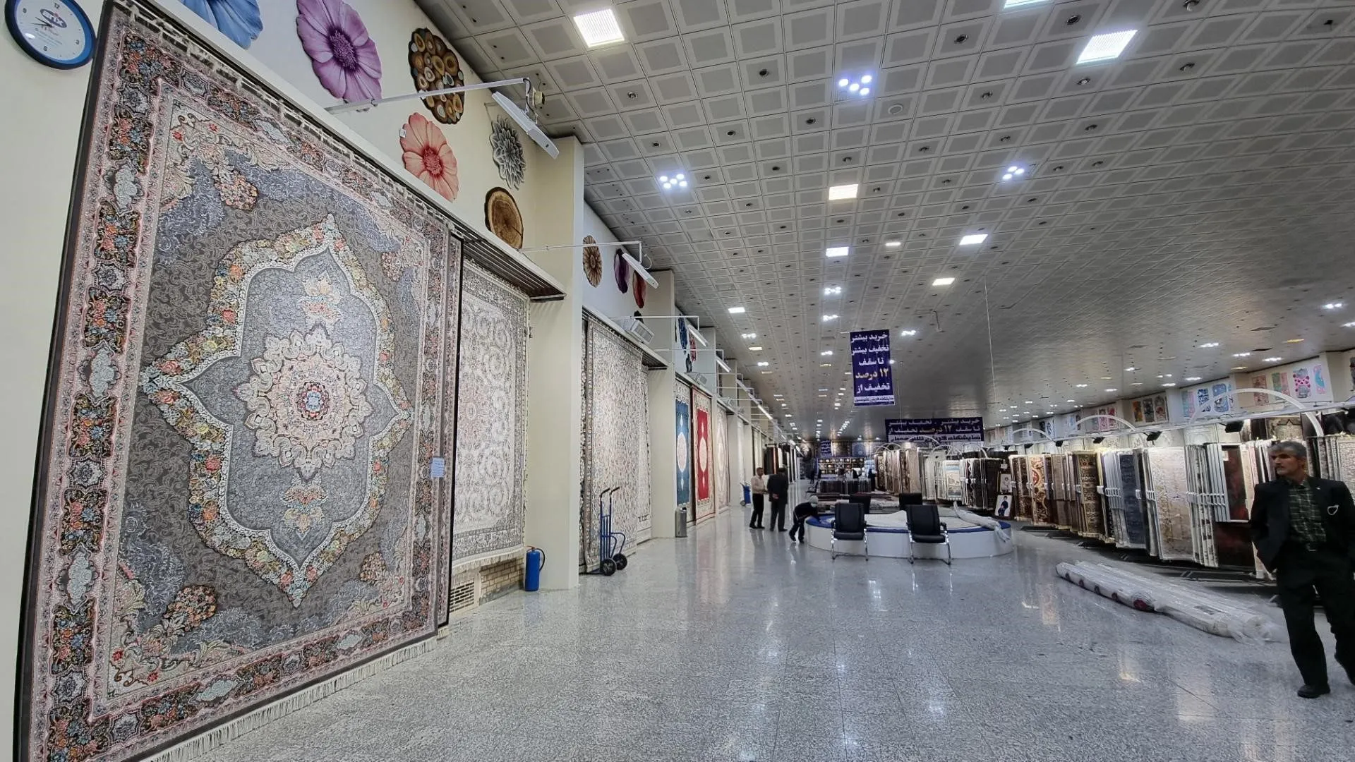 Spacious indoor Persian carpet showroom with intricately patterned rugs hung along the walls and rolled carpets on display
