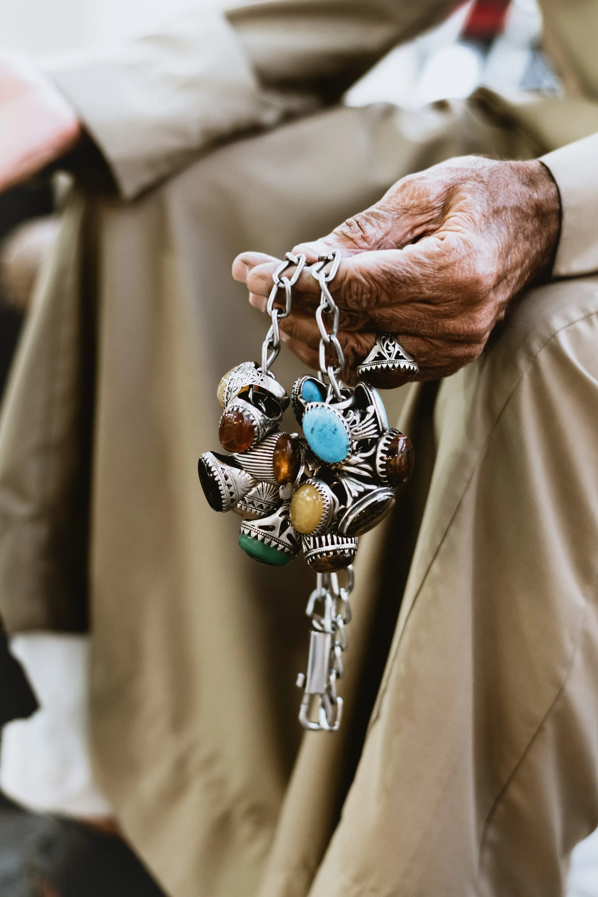 A vendor's hand holding a cluster of hand-made silver rings set with turquoise (firozah), agate (aqiq) and other coloured stones