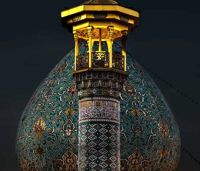 The illuminated dome of the Shah Cheragh shrine in Shiraz at night, covered in intricate turquoise and gold tilework beneath a golden pavilion at its peak