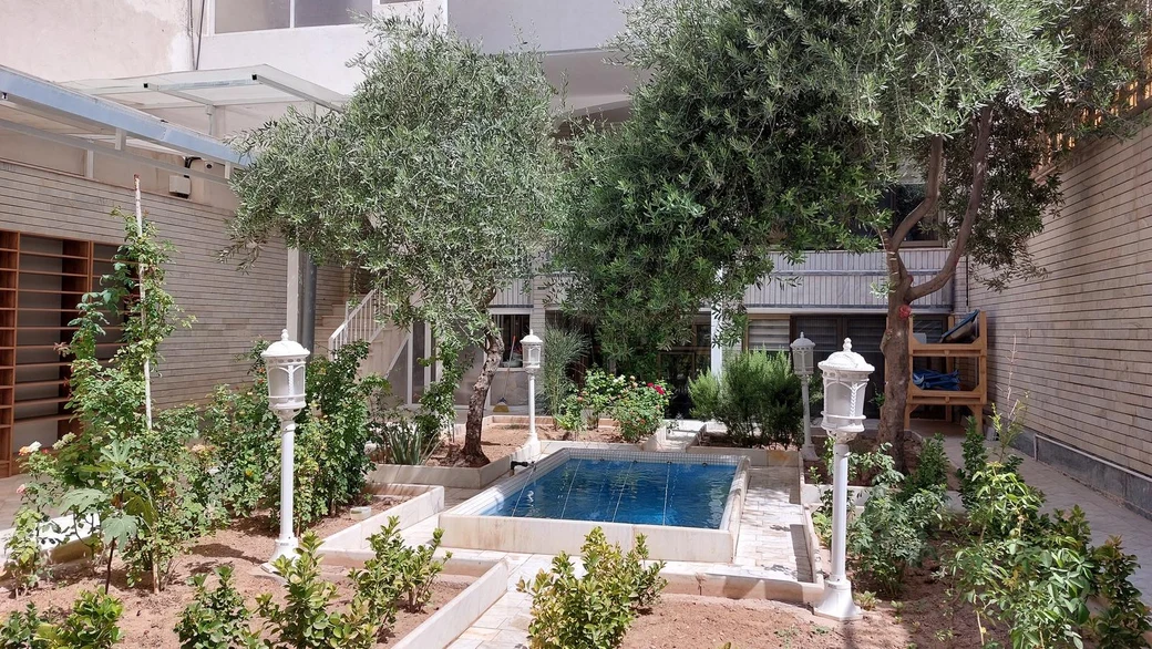 The SIOS courtyard, a sunlit garden with rose beds, olive trees, a small rectangular pool and the school building rising behind