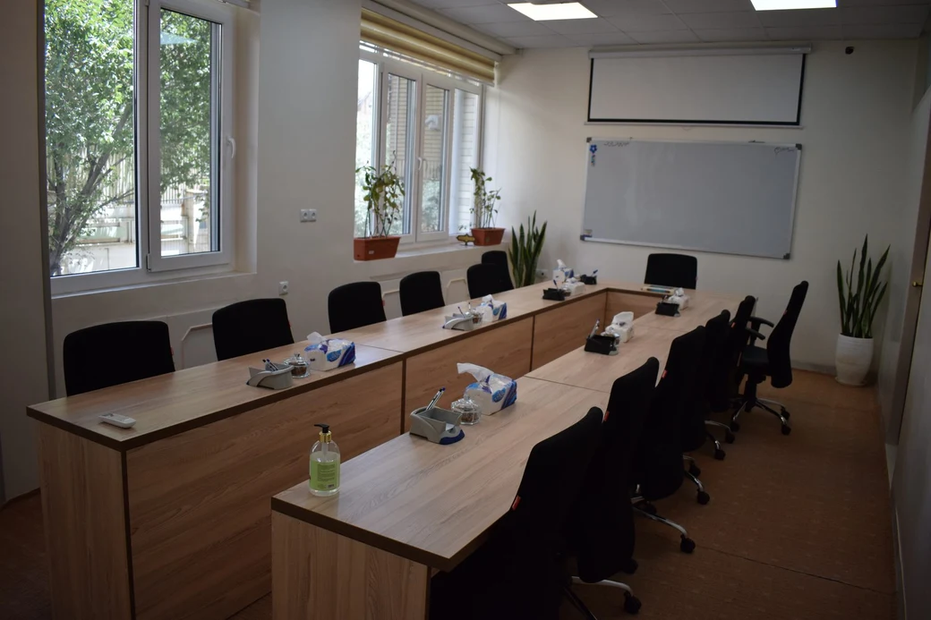 A SIOS meeting room with a large U-shaped wooden conference table, black chairs and a whiteboard and projector screen