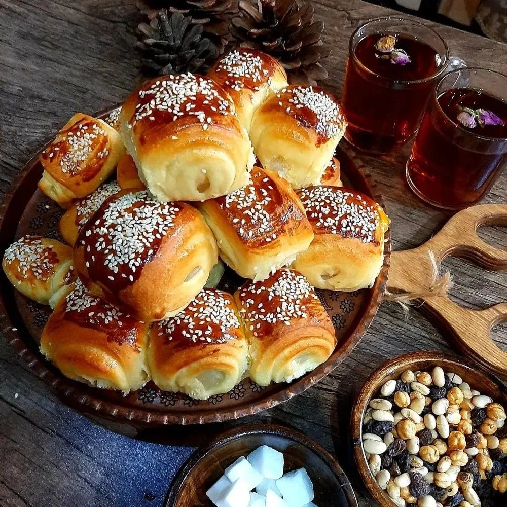 A platter of glazed, sesame-topped Iranian sweet buns served with small glasses of tea, nuts and rock sugar