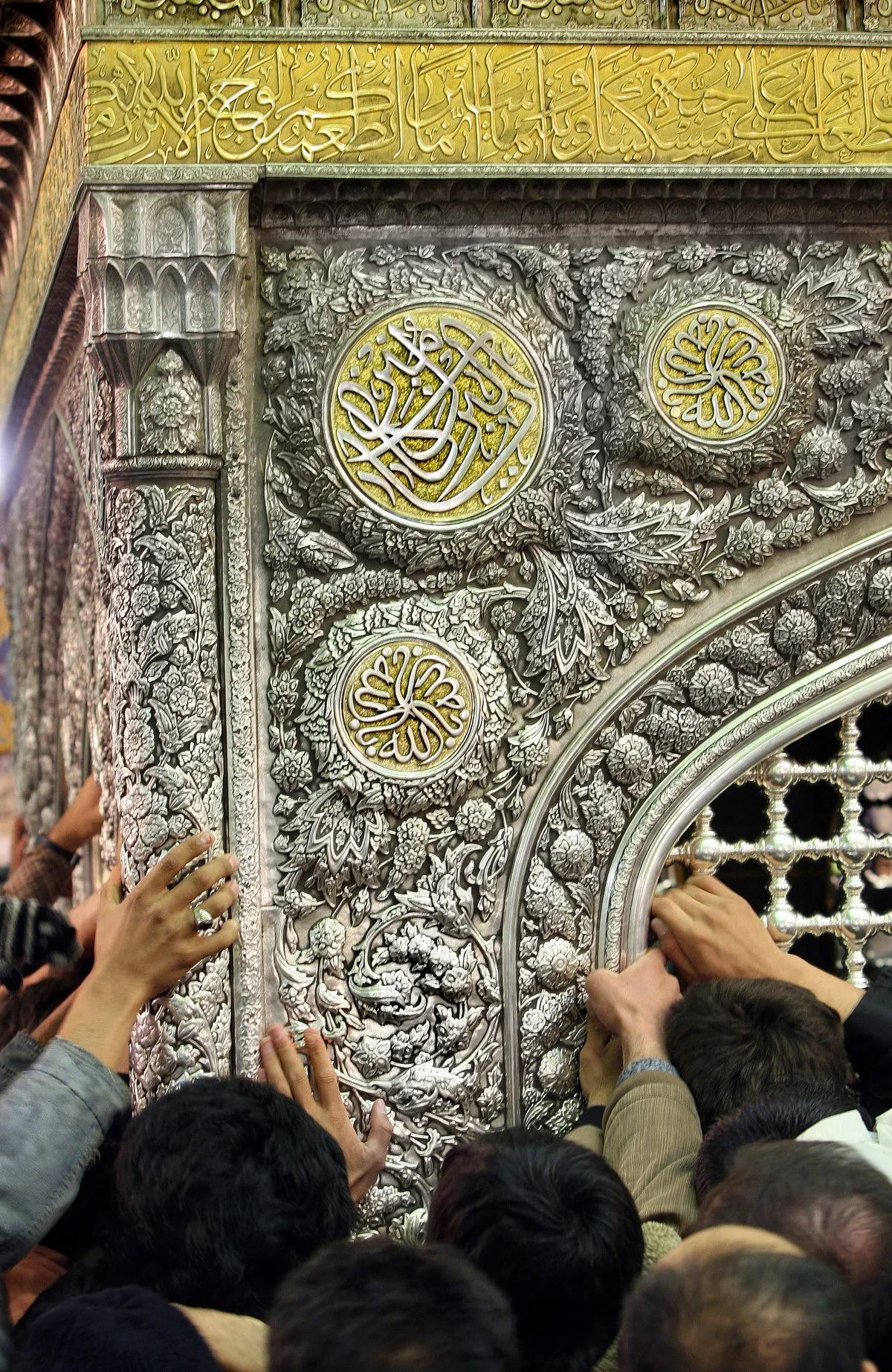 Pilgrims reaching out to touch the ornate silver and gold zarih (lattice) over the grave of Lady Masumah (a) inside her shrine in Qum